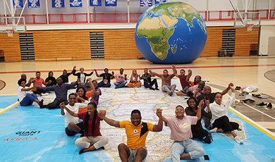 The Mandela fellows hold hands while sitting on a floor map of Africa.