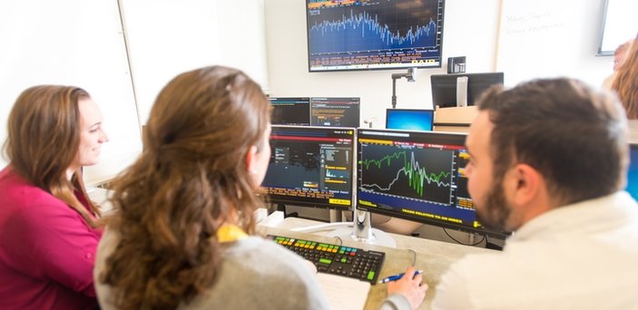 Three students working at a Bloomberg terminal in a classroom